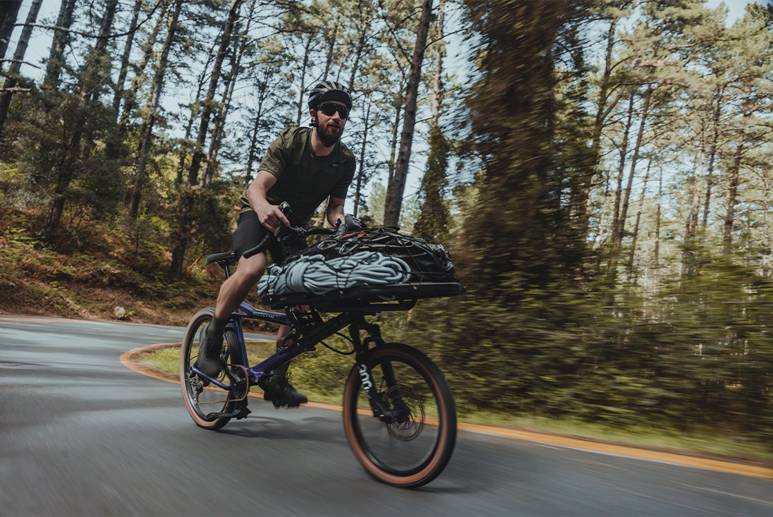A man riding a Hase Gravit Dust cargo and gravel bike on a wooded road. 