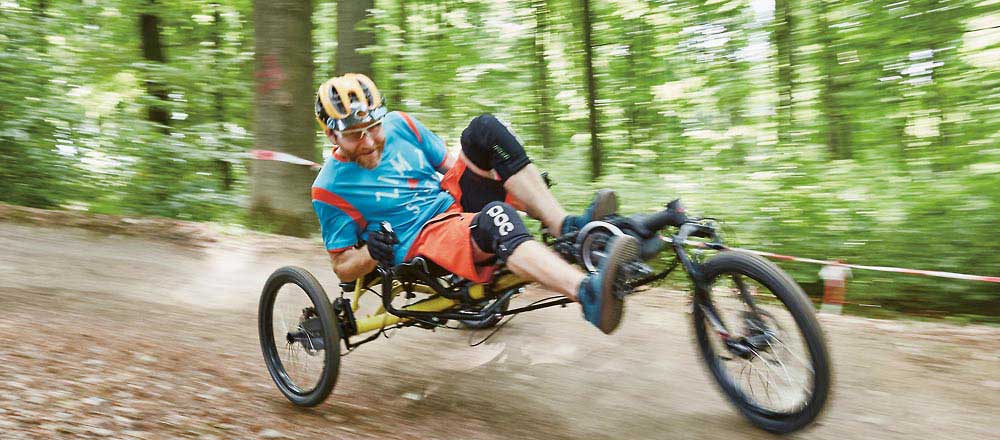 Man riding a Kettwiesel Cross Steps recumbent trike off-road down a hill in the woods