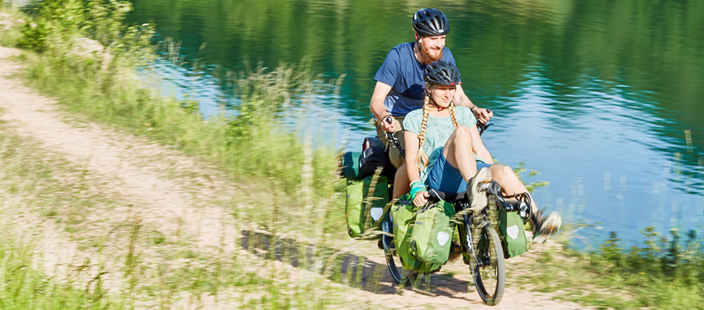 Woman and man riding a Pino Tour recumbent tandem bike with lots of cargo