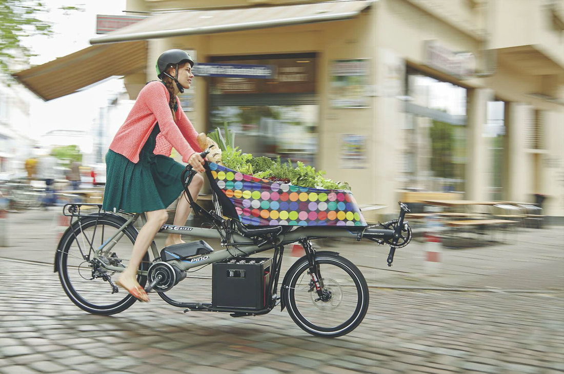 Woman riding a HASE PINO tandem cargo bike with a full load of groceries in the CITY BAG and PORTER RACK