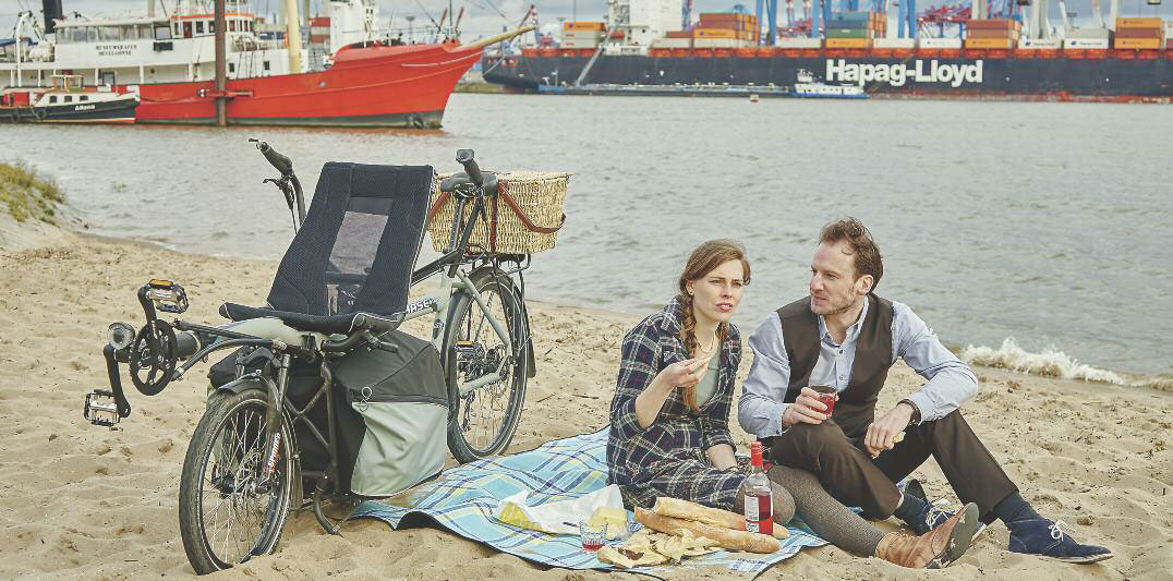 Couple enjoying a beach picnic with a HASE PINO tandem bike standing next to them on its sturdy rack