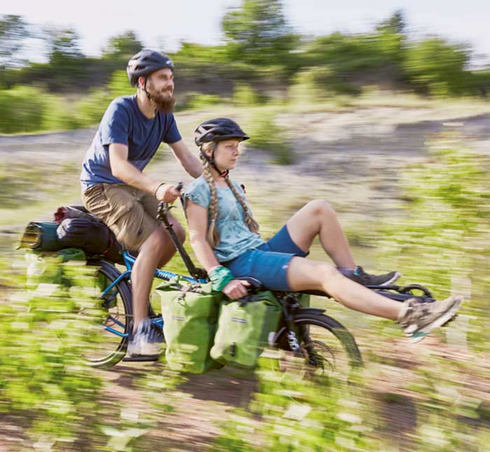 Couple riding a Hase PINO Tour through the brush with cargo bags attached
