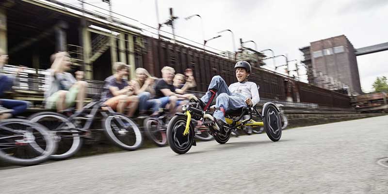 Boy riding a Hase Trix recumbent trike while friends look on